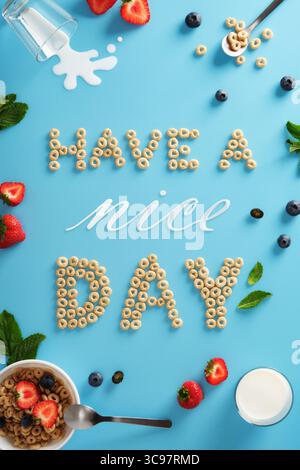 Phrase Have a nice day made from cereal rings with strawberries, blueberries, mint, and spilled milk on blue background. Healthy cheerful breakfast co Stock Photo