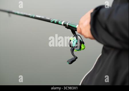 Close-up of adult male hands firmly holding a fishing rod, preparing to cast on a calm lake during a peaceful morning in nature Stock Photo