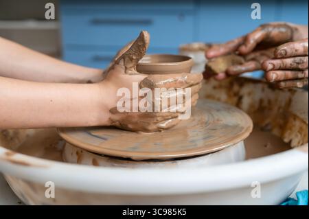 Child and adult hands molding clay together, creating a ceramic cup on pottery wheel, close-up teamwork Stock Photo