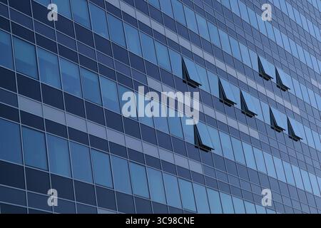 modern high-rise building. The facade is covered with a grid of reflective glass windows, creating a geometric pattern. Some windows are open Stock Photo