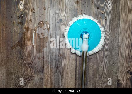 A white mop cleaning a beige floor with a blue handle and liquid on the floor, in natural light and with a glare from a window on the floor, reflectin Stock Photo
