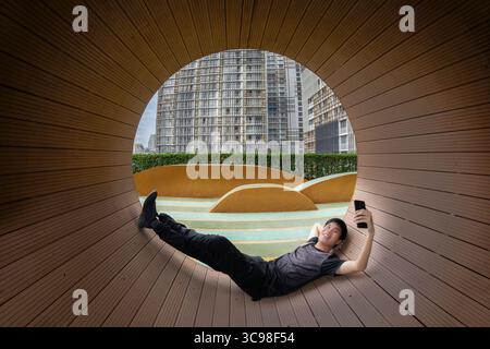 Portrait of young Asian man looking confident and taking a selfie while relaxing and take a nap in a public park. Stock Photo