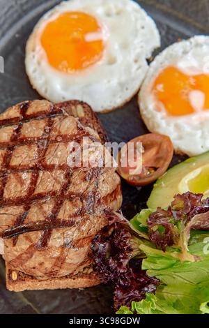Deliciously Grilled Steak Garnished with Fresh Vegetables and Fried Eggs for a Wholesome Breakfast Experience Stock Photo