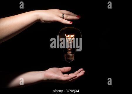 Idea and success concept. Glowing light bulb without wires between female hands on black background Stock Photo