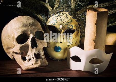Theater and drama concept. Human skull, venetian masks with old scroll on wooden table. Stock Photo