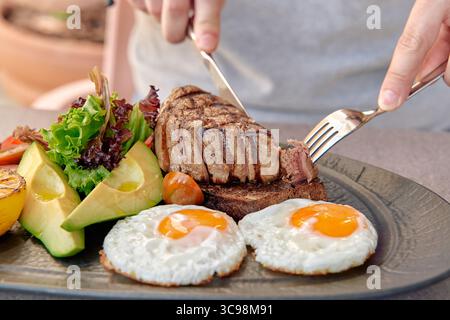A Deliciously Cooked Steak Accompanied by Fried Eggs and Fresh Vegetables on a Stylish Plate in a Culinary Setting Stock Photo
