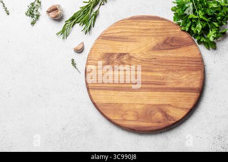 Empty wooden round board with herbs and garlic on white concrete background, top view, copy space. Wooden pizza platter. Food background, design templ Stock Photo