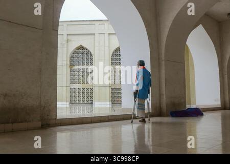 Dhaka, Bangladesh - 10 November 2019: View of an elderly man with crutches standing in the corridor of Baitul Mukarram National Mosque, the gleaming m Stock Photo