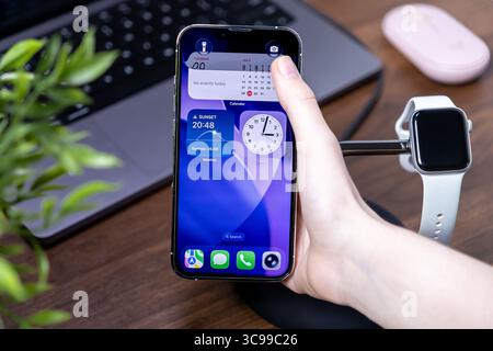 Poznan, Poland - July 29, 2025: A user's hand interacts with a smartphone running ios 26 and Liquid Glass, displaying calendar, clock, weather widgets Stock Photo