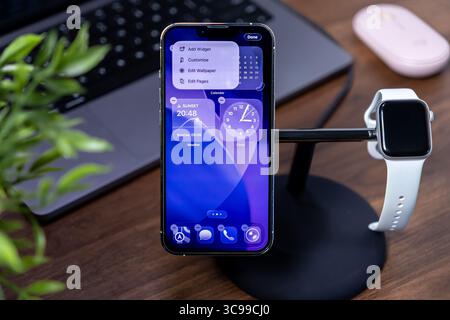 Poznan, Poland - July 29, 2025: Apple iPhone displaying ios 26 Liquid Glass interface with Apple Watch on a stand, highlighting modern connected smart Stock Photo