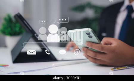 Businessman using smartphone with email, phone, chat and group icons, digital communication and online customer support concept in office setting. Stock Photo
