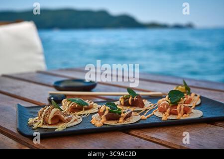 A Beautifully Arranged Platter of Gourmet Seafood Tacos with Fresh Ingredients Served on a Wooden Table by the Ocean Stock Photo