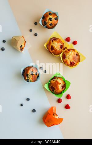 assorted berry muffins—blueberry and raspberry—wrapped in colourful tulip-style paper liners in blue, green, yellow, orange, and neutral tones. Stock Photo
