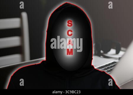 A dangerous hacker in a hood uses a laptop, simulating an urgent message to verify an account as part of a scam scheme, with this scenario potentially Stock Photo