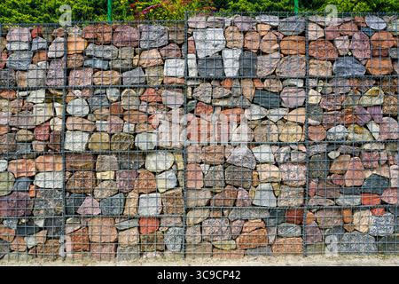 Detailed view of a gabion retaining wall filled with multi-colored stones in a steel mesh grid, used for slope support Stock Photo