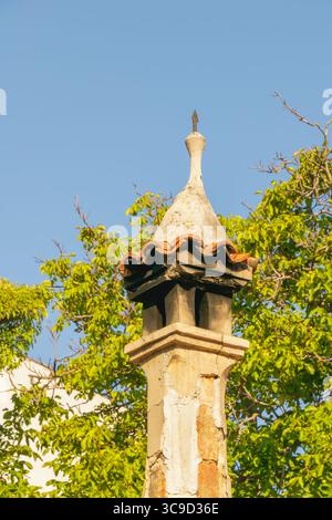 A weathered red brick chimney towers above sloping rooftops, captured from below under a cloudy sky in a historic district. Stock Photo