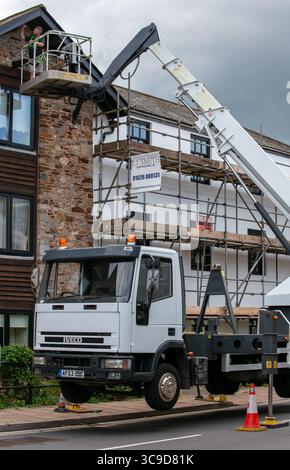 A construction worker on a crane platform working on the exterior of a multi-story building surrounded by scaffolding Stock Photo