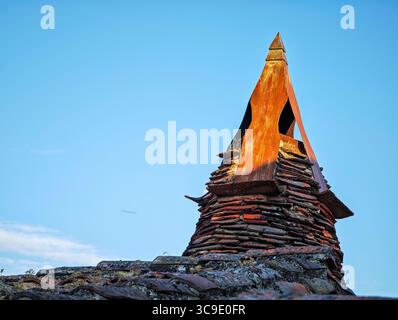 Traditional chimney in Calatañazor features stacked stone and a conical metal hood, showcasing the rustic architecture of the region. Stock Photo