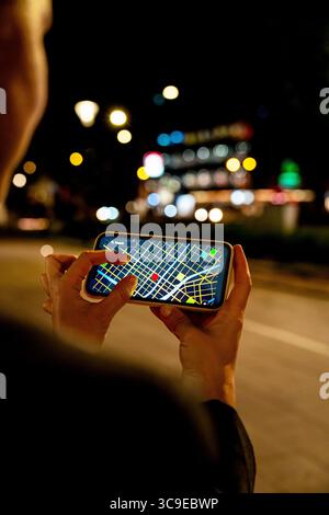 Female person using smartphone for navigation on city street at night Stock Photo