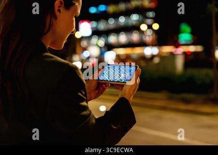 Modern urban female checking GPS map on smartphone outdoors at night Stock Photo