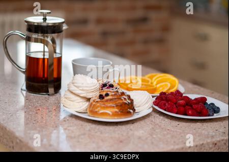 Cozy kitchen scene with teapot, marshmallows, fresh buns and fruits on a countertop, warm homey atmosphere Stock Photo