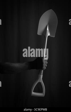 Black and white photo hand holding shovel on dark background Stock Photo