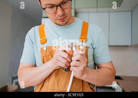 Electrician carefully preparing cable for connecting electric stove using utility knife, working on electrical installation in new modern kitchen during home renovation Stock Photo
