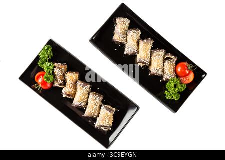 Eggplant rolls with cheese, garlic and sesame on black plates with herbs and tomato. Top view and isolated on white background. Stock Photo