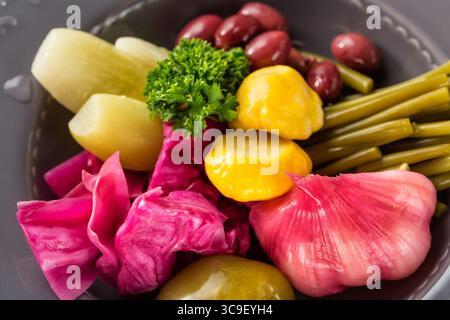 Pickled vegetables in iron plate close up. Garlic wild leek bush pumpkin herbs cucumber cabbage bean. Selective focus. Stock Photo