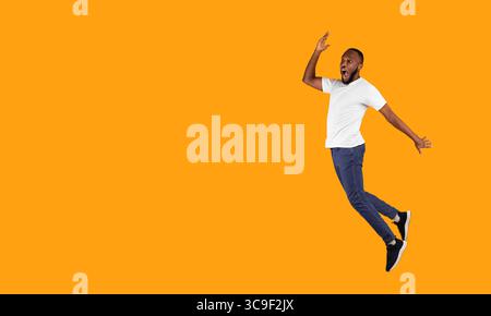 Black Guy Jumping Looking Aside In Shock On Yellow Background Stock Photo