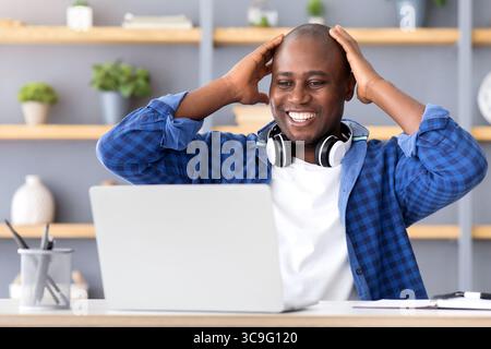 Business success and luck. Excited black businessman looking at laptop computer and touching head in excitement Stock Photo