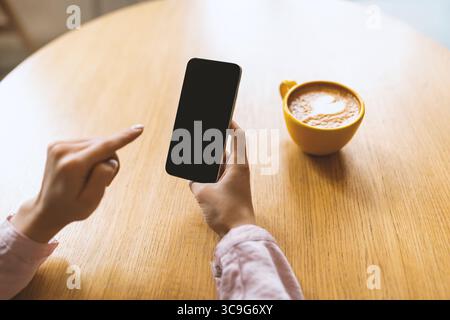 Good start of the day. Young lady holding smartphone with blank screen and drinking morning coffee, sitting in cafe Stock Photo