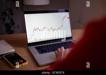 Rearview woman wok on laptop with crypto charts. Investor online tracking digital currency rates Stock Photo