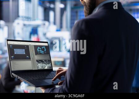 Technician in solar panel facility reviewing photovoltaic system performance on laptop display. Close up of specialist analyzing production metrics on notebook screen to optimize efficiency Stock Photo