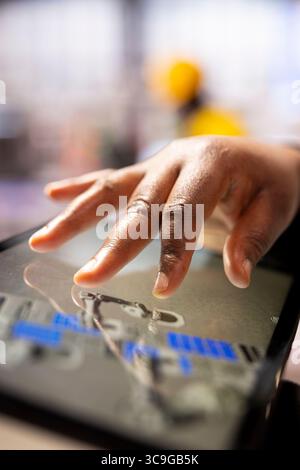 Industry 4.0 engineer programming robotic systems using a CAD software on tablet. African american automation technician utilizing a digital interface to manage smart manufacturing plant equipment. Stock Photo