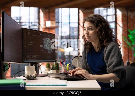 Female IT engineer doing maintenance on artificial intelligence systems, sitting at office desk. Young woman works as a developer with cybernetics and algorithms for machine learning. Stock Photo