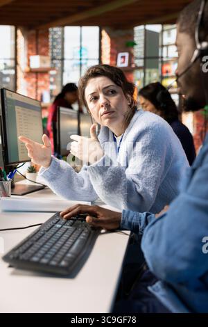 Customer service manager supervising man logging customer interactions in CSM system on computer. Call center supervisor overseeing employee using customer service management software on PC Stock Photo