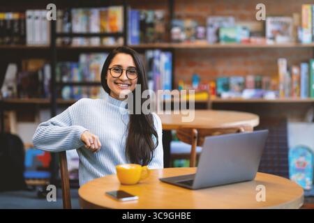 Excited arab woman freelancer working distantly while sitting in cafe and using laptop computer, free space Stock Photo
