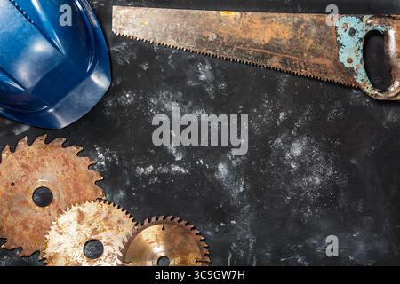 Rusty circular saw blades, saw and safety helmet on dark stone background. Stock Photo