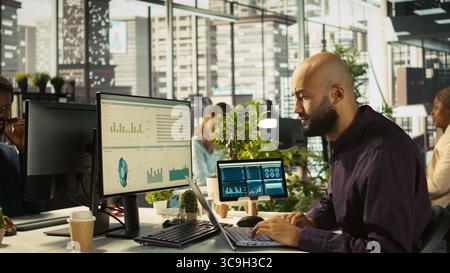 Employee in office celebrating achievement while looking at laptop screen, expressing excitement over successful results. Man happy about positive business accomplishment, camera B Stock Photo