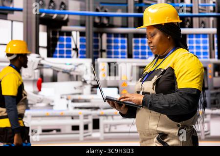 Professional engineer monitors advanced automated system in industrial plant, ensuring seamless robotic manufacturing. African american woman overseeing maintenance of conveyor belt in smart factory. Stock Photo