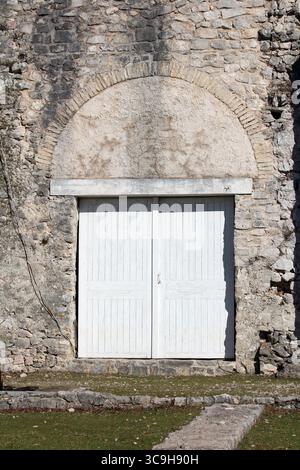 Historic stone wall features an arched lintel above closed double white wooden doors, blending rustic masonry with classic architectural details Stock Photo