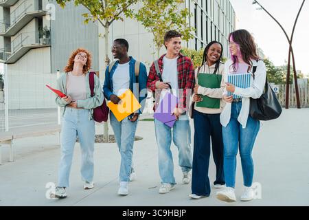 A lively group of young students enjoying their time together, smiling and sharing laughter while carrying vibrant folders and notebooks as they walk Stock Photo