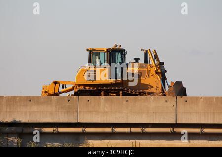 A large yellow bulldozer stands idle atop a concrete overpass, its tracks and blade visible, symbolizing heavy machinery at work in modern infrastruct Stock Photo