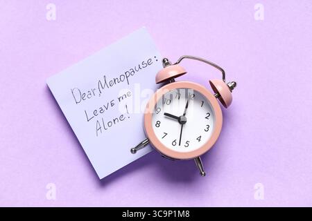 Paper with text DEAR MENOPAUSE LEAVE ME ALONE and alarm clock on lilac background Stock Photo