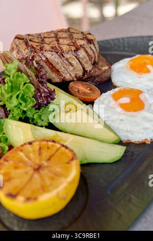 A Delicious Plate Featuring Grilled Steak, Fried Eggs, Fresh Vegetables, and Sliced Citrus for a Perfect Brunch Experience Stock Photo