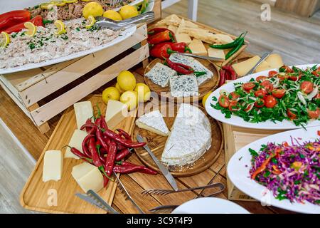 A Vibrant Display of Fresh Ingredients and Gourmet Dishes Featuring Various Cheeses, Salads, Peppers, and Citrus Fruits on a Wooden Table. Stock Photo