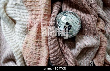 Disco ball lies on soft material. Knitted fabric is chaotically folded into different folds. Different knitting textures. And different pastel colors Stock Photo
