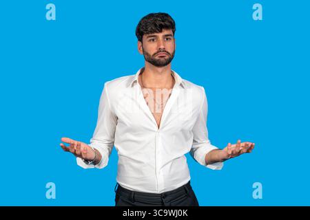 Young man in white shirt gesturing with open hands against blue background Stock Photo