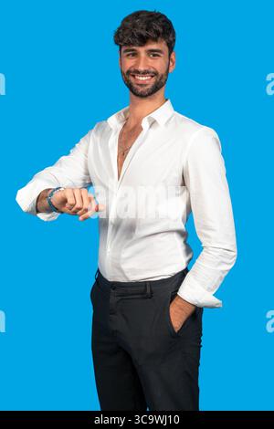 Smiling man in formal attire checking time against a blue background Stock Photo